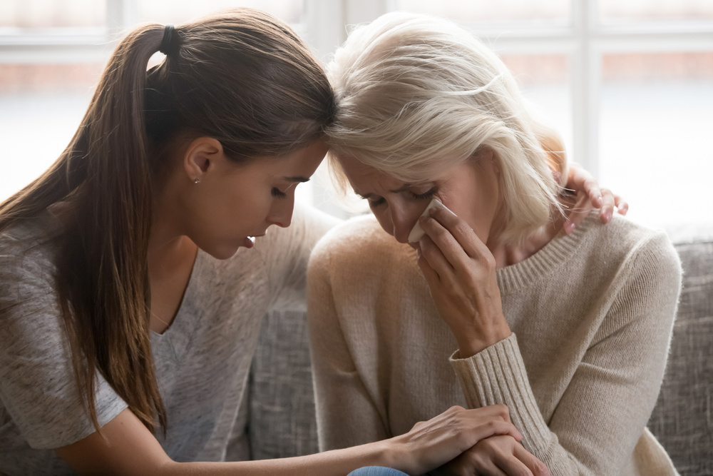 Grownup daughter soothe aged mother holds her hand feeling empathy